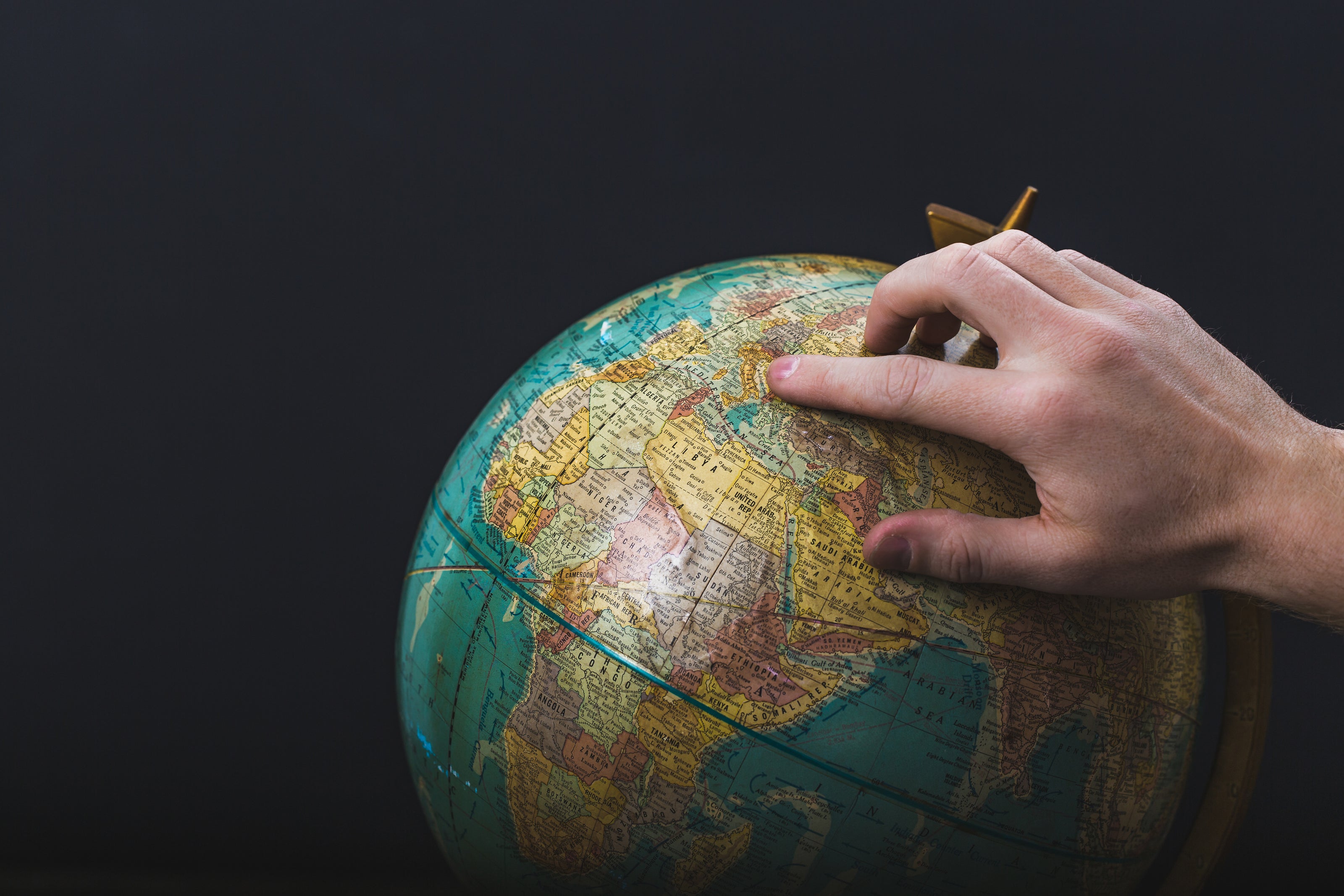 Hand pointing at a terrestrial globe, travel